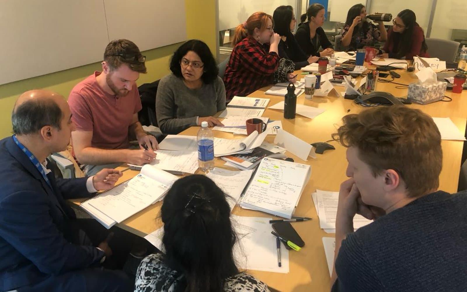 A small group working through course material around a table, notebooks and worksheets open in front of them, a trainer sitting in with them.