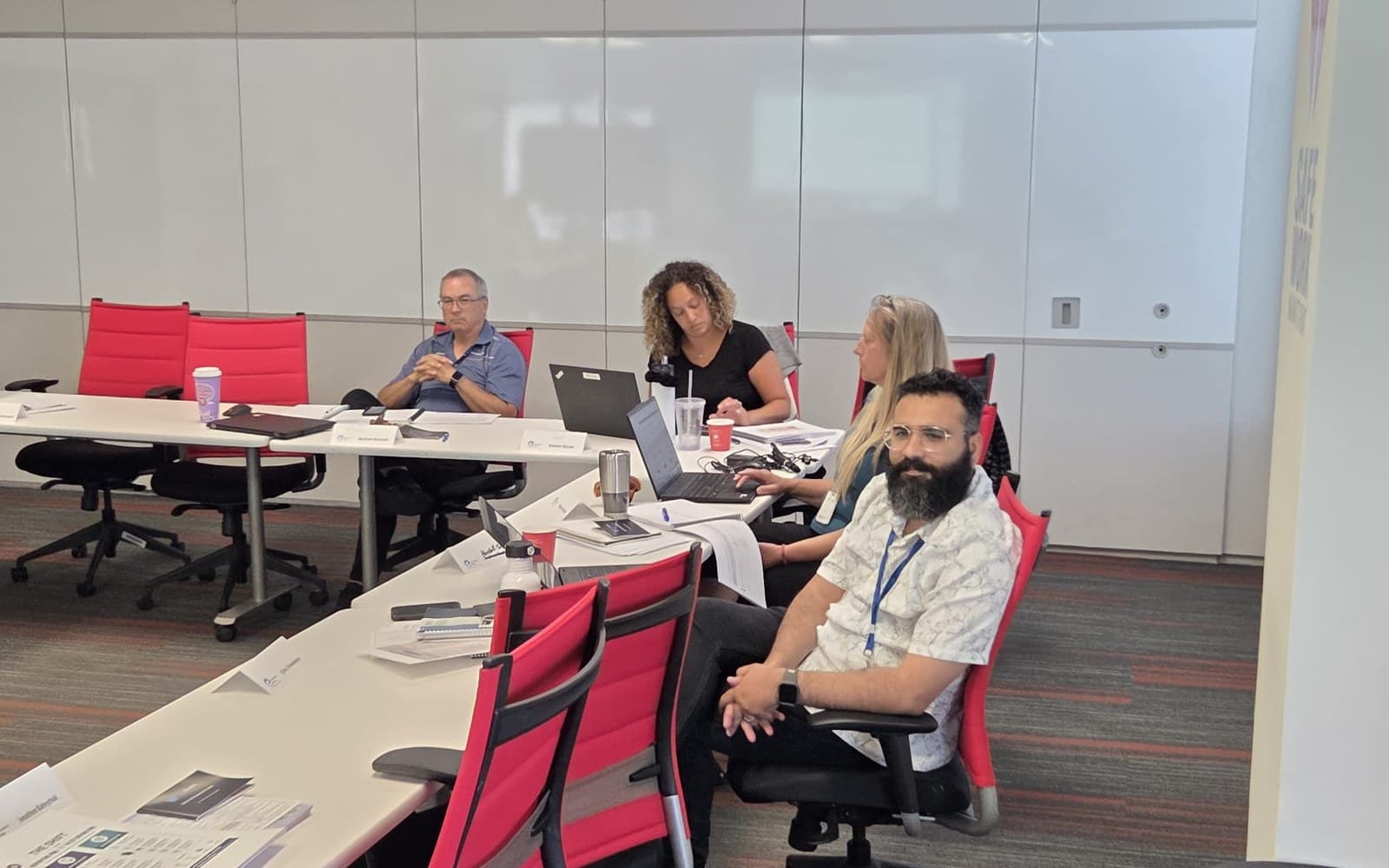 Four participants seated along a training-room table with laptops and notes, listening to the session.