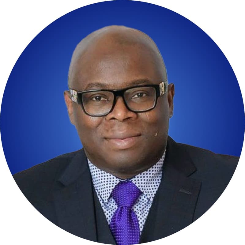 Dave Odigie, in a dark suit and purple tie, photographed against a blue background.