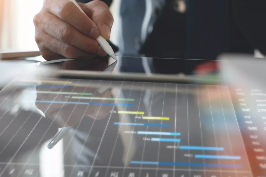 Hand using a stylus to analyze a digital Gantt chart on a tablet, representing project planning in PMP certification