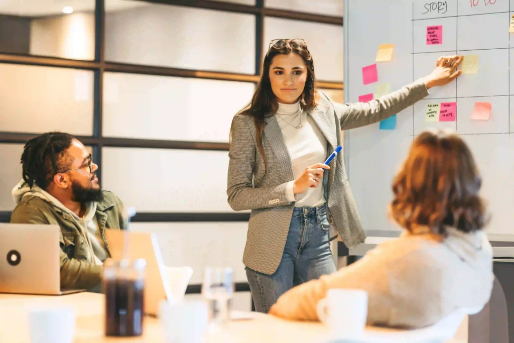 Female trainer conducting a PMP training session using an Agile board with sticky notes, while team members listen.
