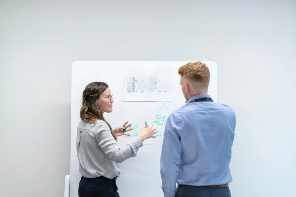 Two professionals analyzing a whiteboard diagram, emphasizing the detailed planning and timeline required to complete PMP certification.