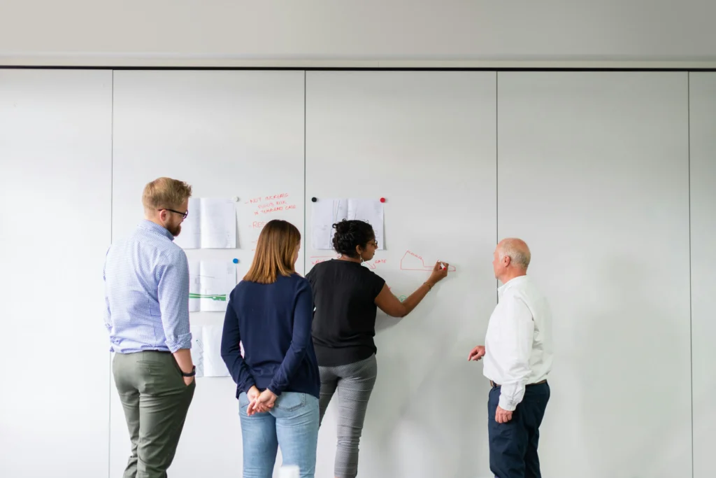 Group of professionals collaborating around a whiteboard, discussing strategies to maintain PMP certification and career growth.